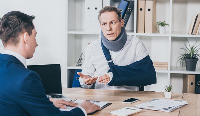 A man wearing a cervical neck brace and an arm sling sitting at a desk, discussing legal matter