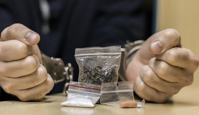 A person in handcuffs sitting with three different drug in plastic packet