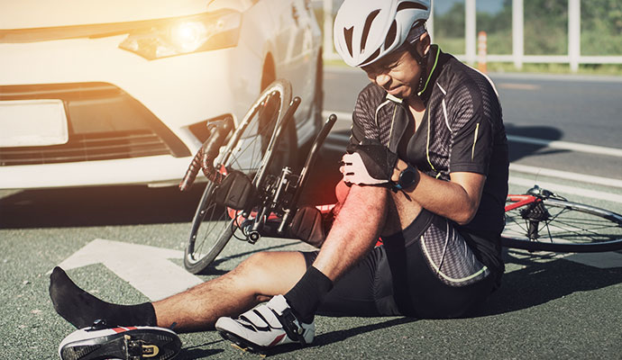 A cyclist sitting on the road holding an injured knee