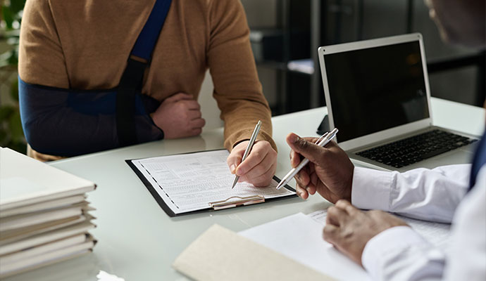 A person with their arm in a dark blue sling meeting with a professional at a desk