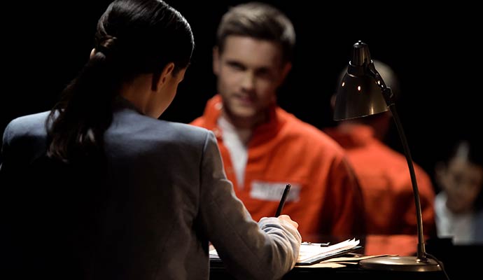 Professional woman taking notes at a desk while facing a prisoner in an orange jumpsuit