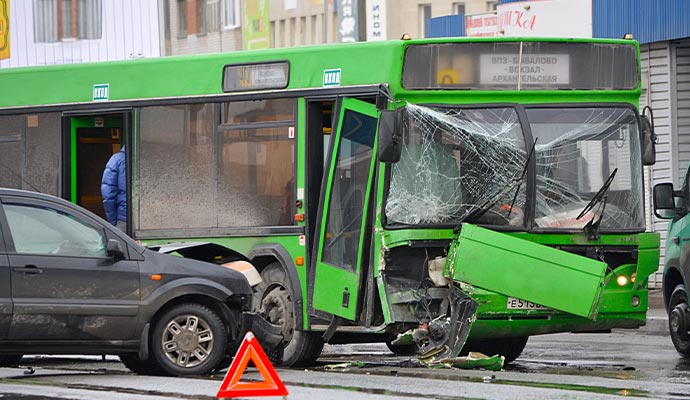 A green passenger bus and a dark car that have collided at an intersection