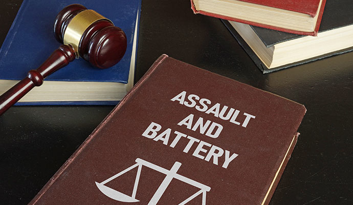 Law book titled assault and battery with a gavel and stacked books on a desk