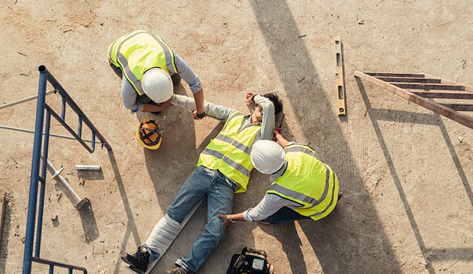 An overhead view of a construction worker lying on the ground and two colleagues are provide immediate assistance